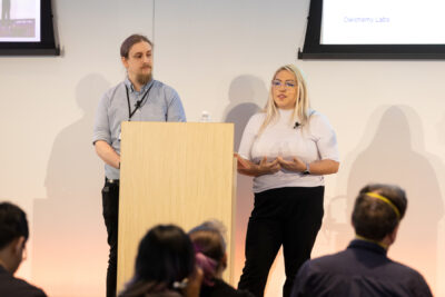 Jazmin Cano and Peter Galbraith stand behind podium while presenting Loud and Clear presentation