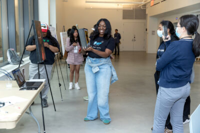 Denise Coke smiles and stands in the demo hall holding the physical component of her augmented reality art