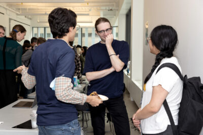 Three people are talking over lunch. One man partially hides his smile behind his hand.