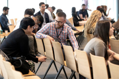 A man smiles as he twists in his seat to chat with the person behind him.