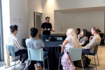 Jamie Bykov-Brett addresses a small breakout session group, standing while the members of the breakout look up attentively