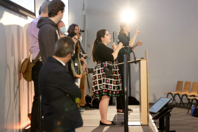 Danielle Montour stands behind the podium holding her white cane, with the breakout session leaders arrayed behind her. Viewed from the side.