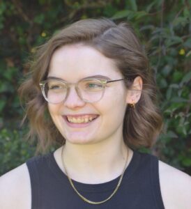 Headshot of Amy Crighton, a very pale white woman with brown hair in a bob, clear framed glasses and a black sleeveless top on. She smiles off to the side.