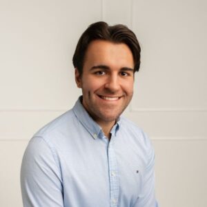 Headshot of Anis Idrizovic, a white man with wavy brown hair and a wide smile wearing a light blue dress shirt.