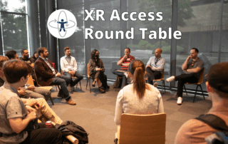 XR Access Round Table. A group of people sit in a circle of chairs during the 2024 XR Access Symposium, having a breakout discussion.