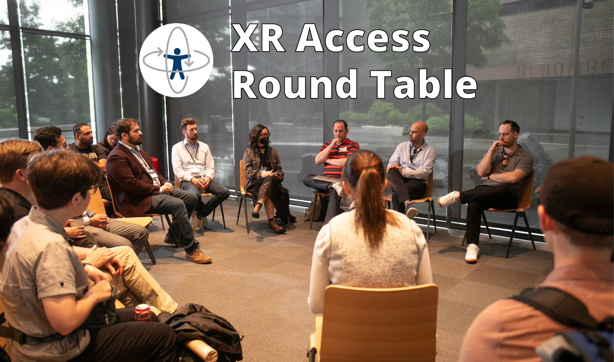 XR Access Round Table. A group of people sit in a circle of chairs during the 2024 XR Access Symposium, having a breakout discussion.