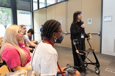 A light-skinned, female audience member using a walker stands up to ask a question.