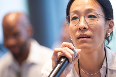 Closeup of a female Asian audience member asking a question into the microphone, her attention fixed on the stage.