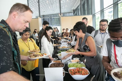 Attendees eagerly gather food from the lunch buffet, a taco bar loaded up with meat, mushrooms, lettuce, salsa, and a bevy of colorful foods and toppings.