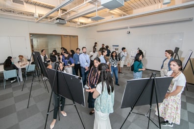 In the poster room, many attendees gather around 2 foot by 3 foot informative displays.