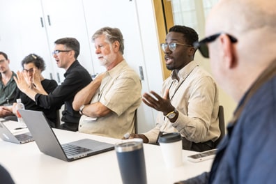 Michael Bervell, one of the XR/AI Policy and Standards leaders and a black man with short dark fuzzy hair and goatee, gestures and speaks to the table.