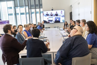 Around 18 people sit around a long conference table for the XR/AI Policy and Standards breakout discussion. A monitor at the far end shows the feed being broadcast to Zoom.