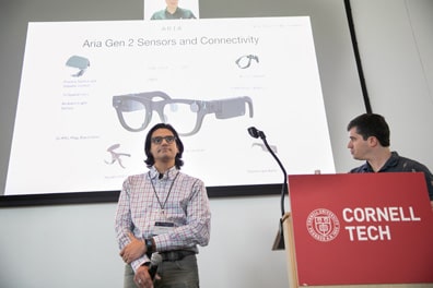 Agustya Mehta, a dark-skinned man with neatly combed hair and thick glasses, stands in front of a slide from his talk AI Advancement in Wearable and MR Technology. The screen behind him shows Meta’s new Aria Gen 2 smart glasses and breaks down its sensors.