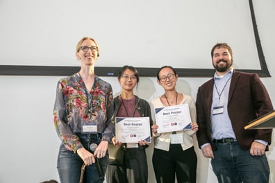 XR Access leaders Dylan Fox and Shiri Azenkot present the Best Poster certificates to winners Lynn Xu and Chelsea Twan for their work on 'Empowering Inclusive Care: An Immersive VR Training Program for Neurodiverse Patient Interactions.' Lynn is a light-skinned woman with black/brown hair just past the shoulders wearing a black jacket over a dark red shirt, while Chelsea is a tan-skinned woman with long black hair wearing a white sweater.
