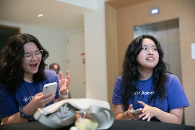 Two volunteers wearing XR Access T-shirts laugh in excitement at something on their phones.