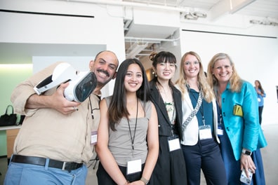 A row of people smile for the camera in the exhibition all, the leftmost holding a VR headset.