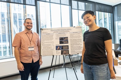 Shuxu Huffman and Abraham Glasser of Gallaudet University stand proudly next to their poster “Exploring Virtual Reality to Mitigate Visual Split in Computer Science Education for Deaf and Hard of Hearing Classrooms.” Shuxu is an Asian person with short hair and glasses wearing a black T-shirt and jeans; Abraham is a light-skinned white male with short curly brown hair wearing a salmon-colored collared shirt.