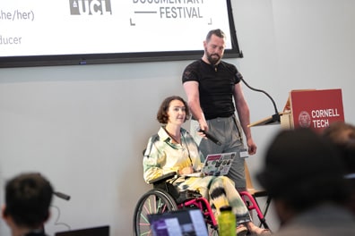 Meg Fozzard, a white woman with short curly hair in a hot pink wheelchair, presents from Cripping Up – How we are Using VR to Challenge Ableism.