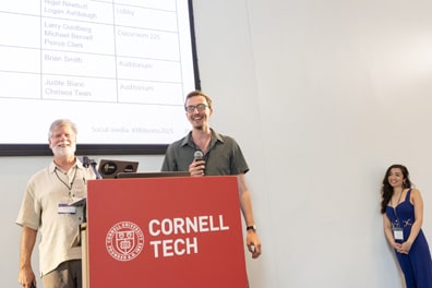 Larry Goldberg, a white man with gray hair and beard, and Peirce Clark, a younger white man with short brown hair, smile from the podium. As co-leaders of the XR/AI Standards and Policy breakout, they share about their intentions for the discussion.