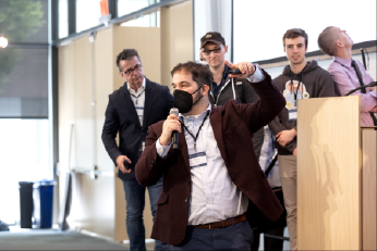 Dylan Fox gestures emphatically at an XR Access Symposium as speakers look on behind him